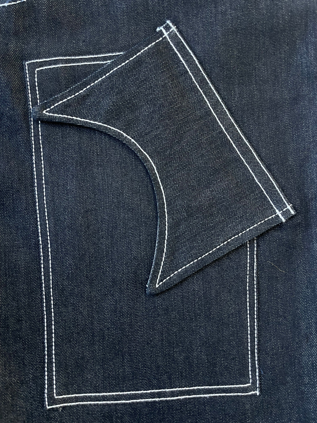Denim fabric side pocket with a white stitching pattern on a dark denim background