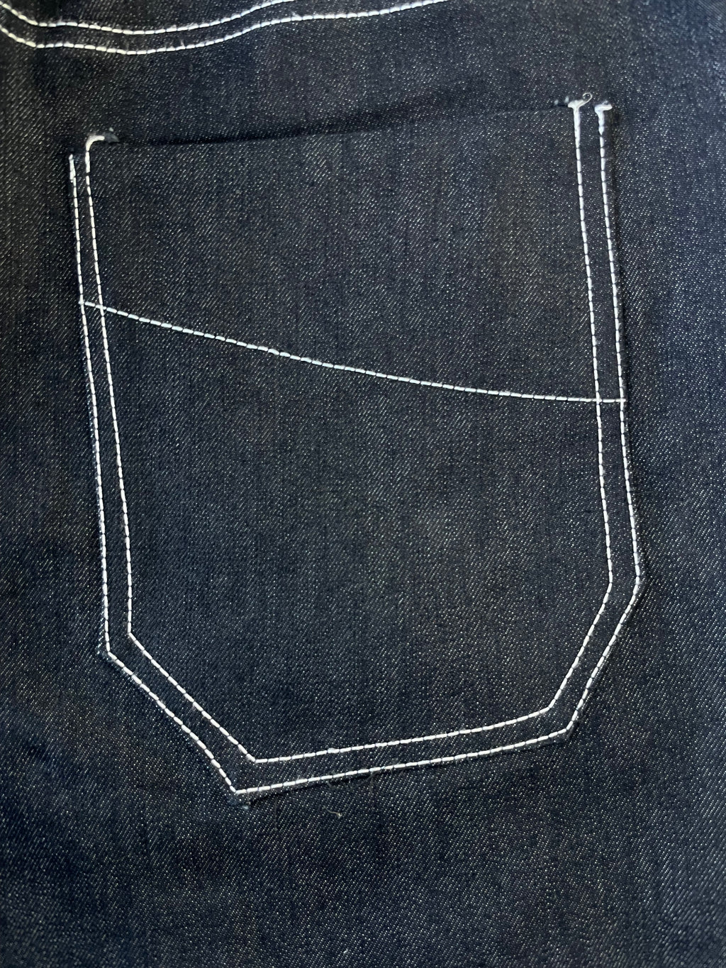 Close-up of a dark fabric pocket with white stitching on a matching fabric background